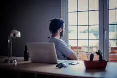 Man with his back to his desk, looking out a window.