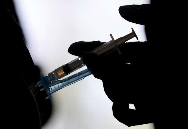 A medical practitioner injects a COVID-19 vaccine into the arm of a patient. 