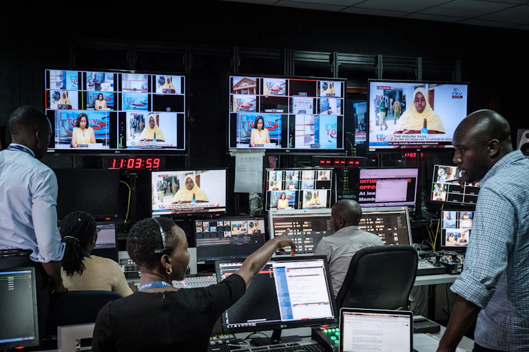People sitting and standing in front of computers and television screens in a control room