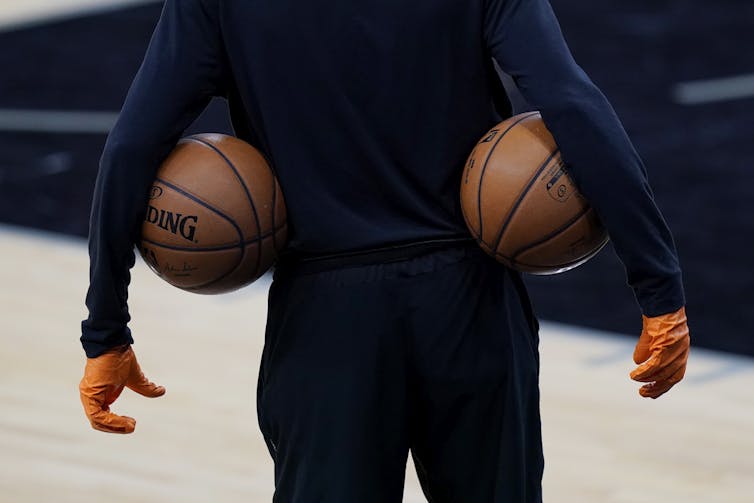 A man wears gloves and has a basketball tucked under each arm.