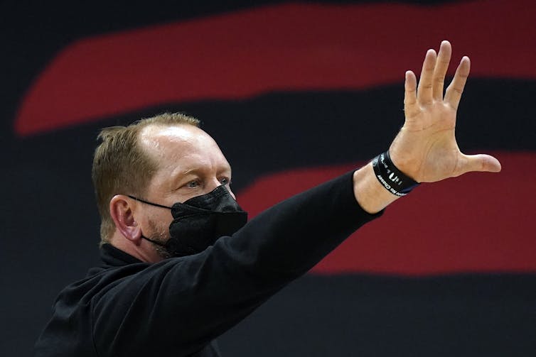 Toronto Raptors head coach Nick Nurse, wearing a mask, raises his hand as he calls a play