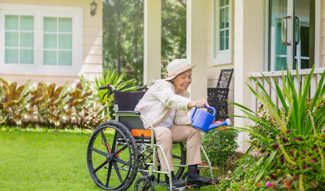 Elderly woman in a wheelchair watering garden outside her unit