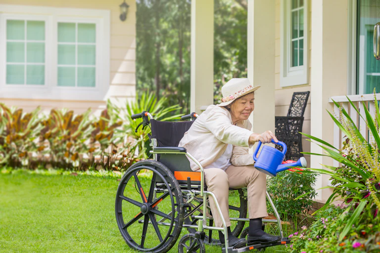 Elderly woman in a wheelchair watering garden outside her unit
