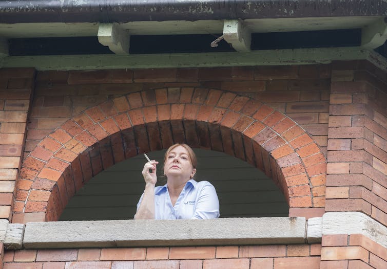 Woman smokes on balcony.
