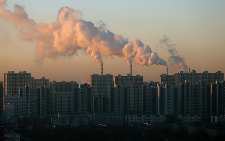 Smoke billows from a coal-fired powered station behind a city skyline.