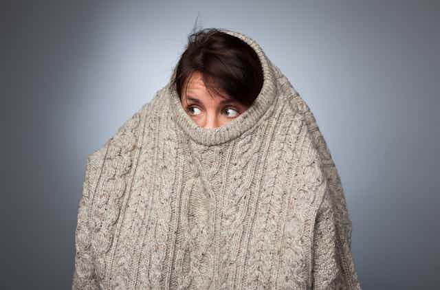 A woman hides within a big jumper looking slightly scared