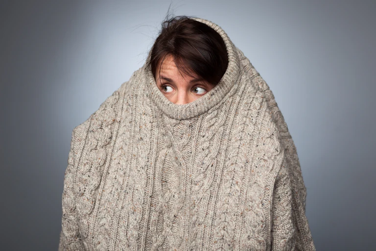 A woman hides within a big jumper looking slightly scared