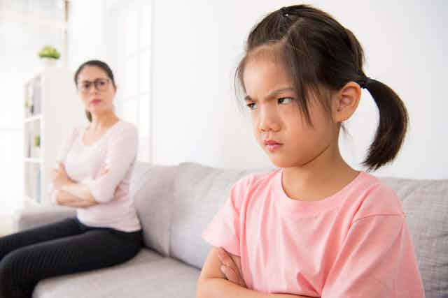 A child crosses her arms in anger as a woman looks on 