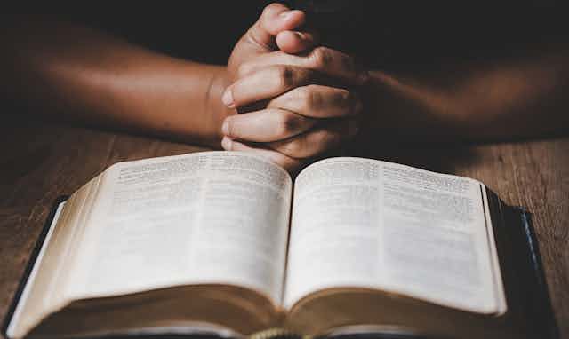 Praying hands in front of an open Bible.