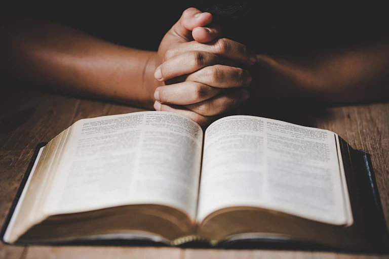 Praying hands in front of an open Bible.