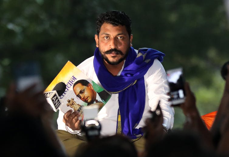 Indian man with moustache and scarf holding political posters at a protest rally in Delhi October 2020.