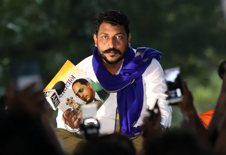 Indian man with moustache and scarf holding political posters at a protest rally in Delhi October 2020.