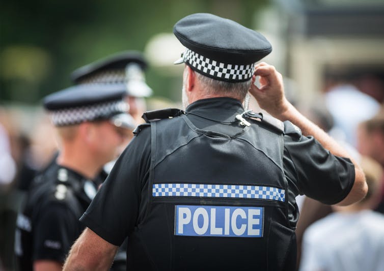 Back of police officer who listening to his in-ear radio.