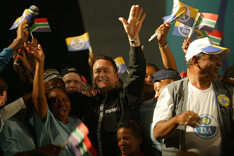 A smiling man raises his arms, surrounded by people waving miniature flags.