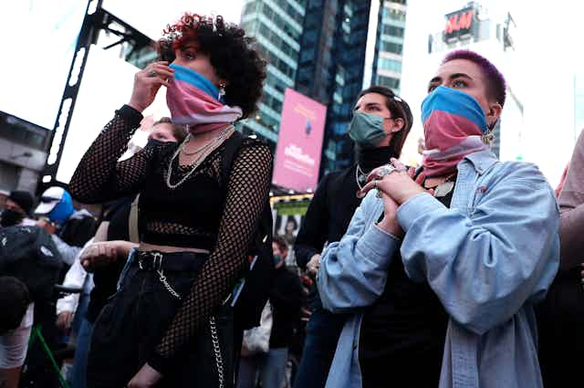 People wearing transgender pride flags as face masks listen to speeches during a demonstration in Times Square