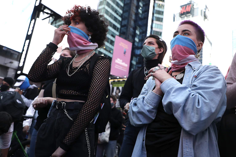 People wearing transgender pride flags as face masks listen to speeches during a demonstration in Times Square