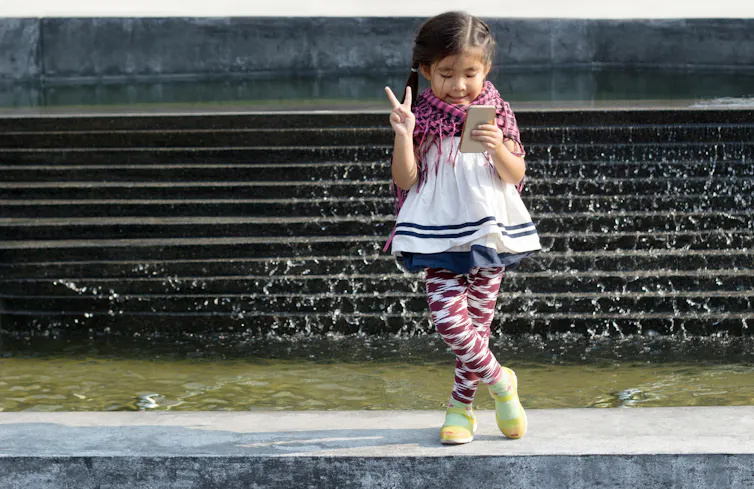 Young girl looking at her smartphone and making peace sign.