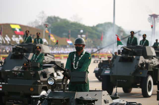 Soldiers drive tanks bearing Myanmar flags down a public street