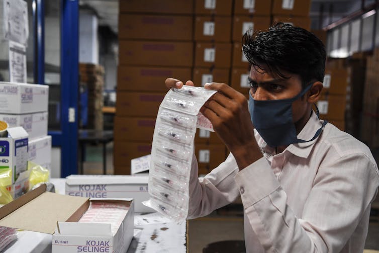 A worker looks closely at a series of packaged syringes