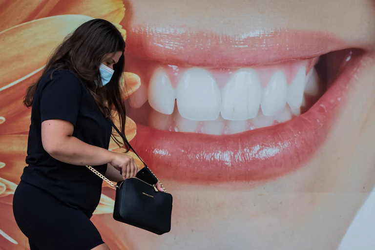 A woman in a face mask walking past a large close-up photo of a smiling mouth