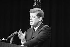 President John F. Kennedy gestures with his right hand as he speaks in front of a lectern in 1962.