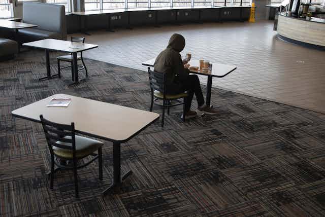 A student sits alone in a university cafeteria.
