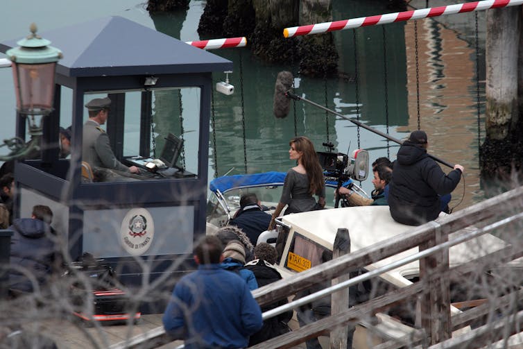 Angelina Jolie em um barco em um canal de Veneza, cercada por membros da tripulação