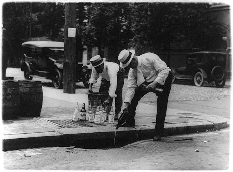 Men pour bottles into a storm drain