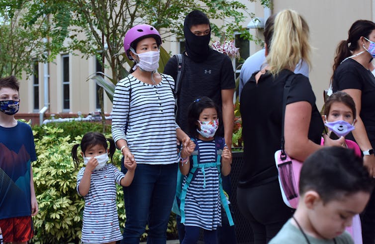 An Asian American family wearing masks stand together.