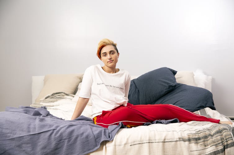 A gender-nonconforming person sits on their bed