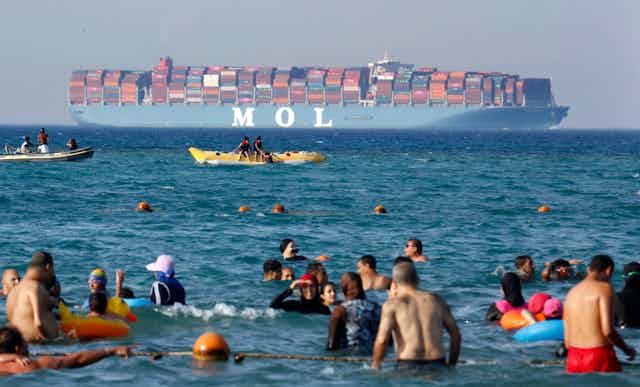 People bathe in the sea near an Egyptian beach as a large container ship passes by in the distance