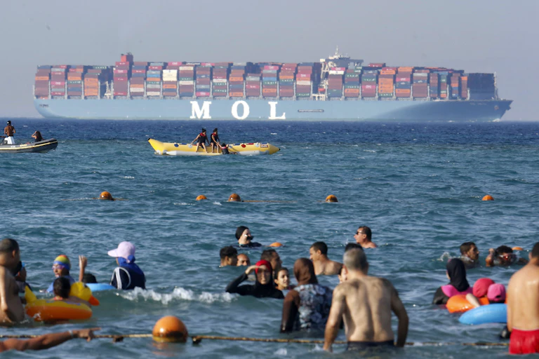 People bathe in the sea near an Egyptian beach as a large container ship passes by in the distance