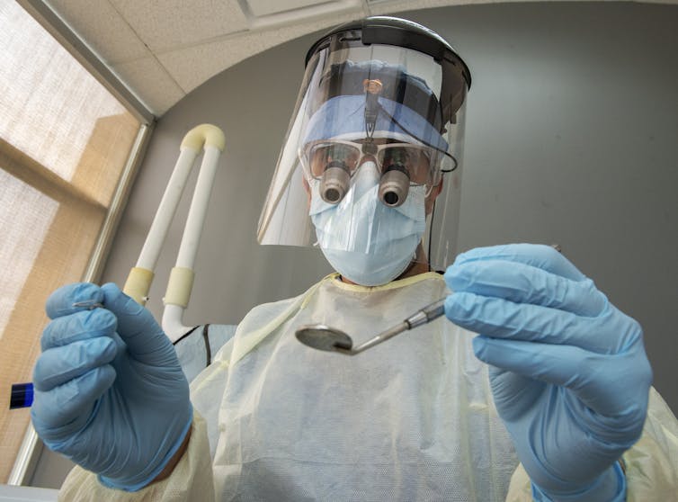 A dentist wearing PPE: gown, mask, face shield and gloves.