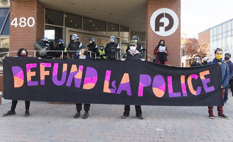 Protesters hold up a sign that says Defund La Police.