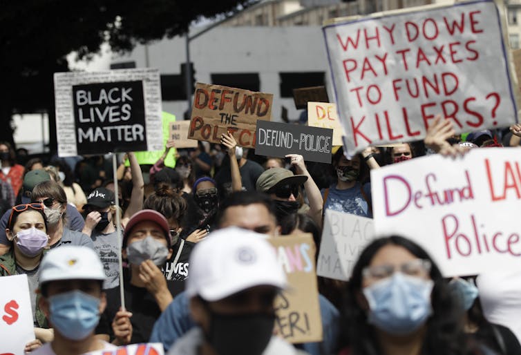 Protesters carry defund police signs.