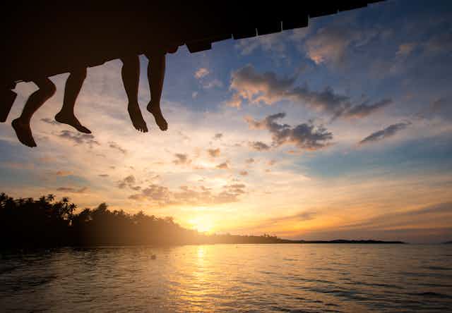 silhouette of legs dangling from a bridge at sunset over a lake