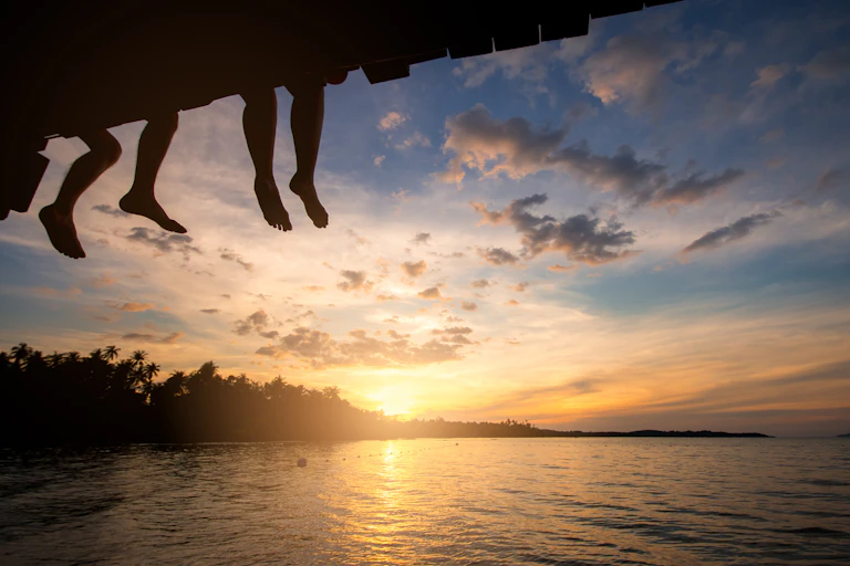 silhouette of legs dangling from a bridge at sunset over a lake
