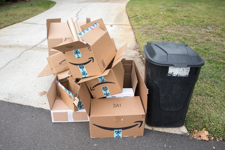 a pile of amazon boxes next to a garbage can at the curb