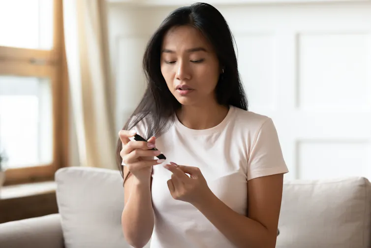 A woman tests her blood sugar by pricking her finger.