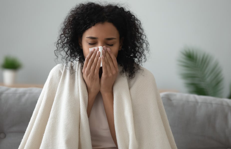 A woman with a blanket over her shoulders blowing her nose.