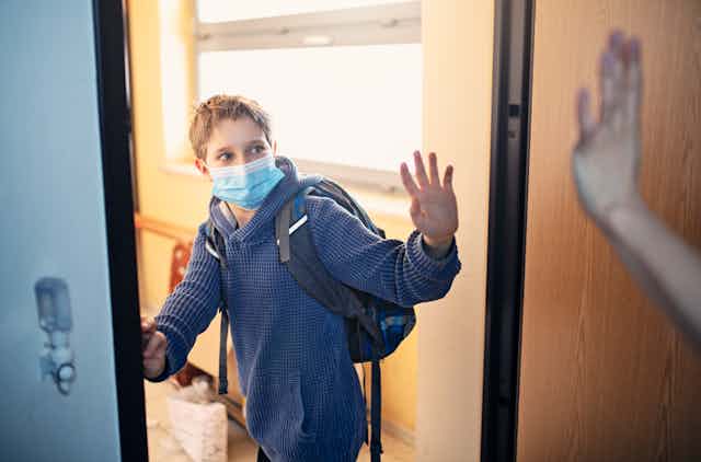 masked boy in backpack waves entering room