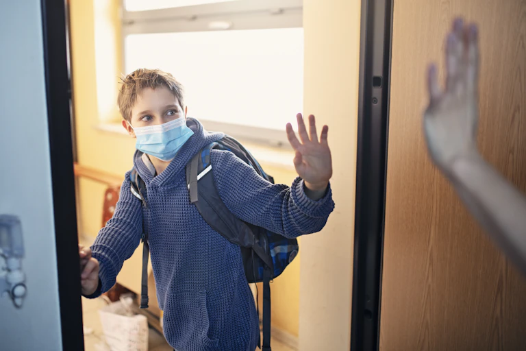 masked boy in backpack waves entering room
