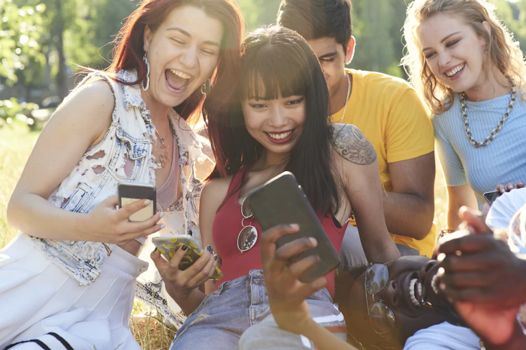 Five young adults looking at their phones and laughing.
