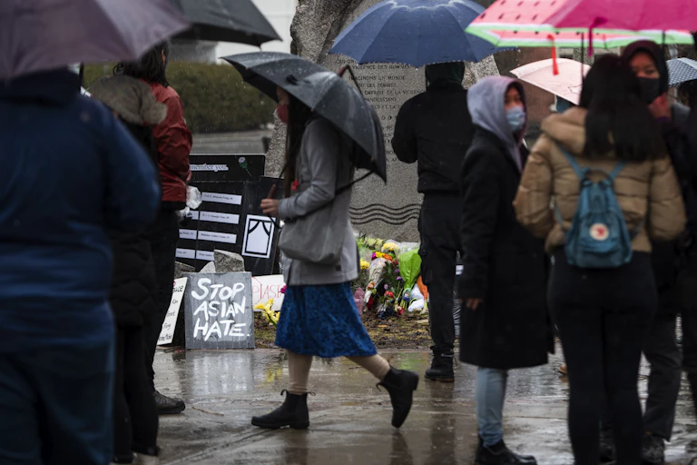 People standing in front of a monument with signs reading 'Stop Asian Hate'
