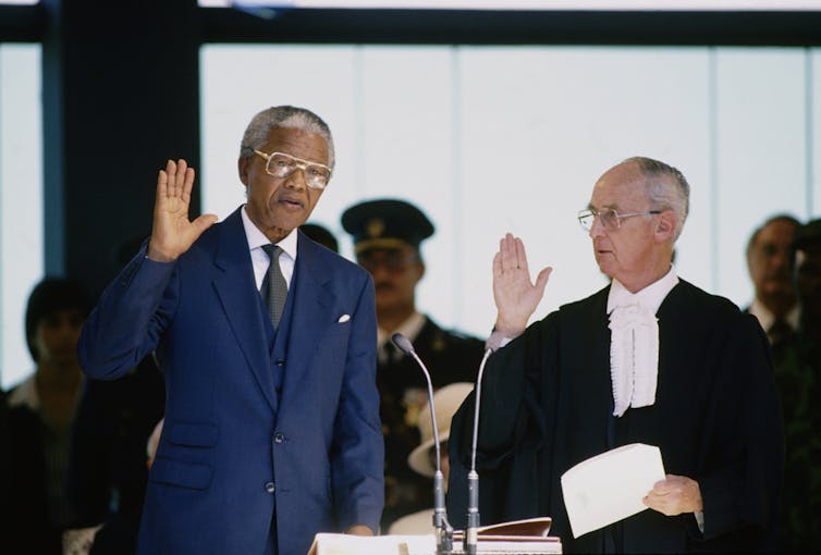 Mandela holds his right hand in the air, next to a judge