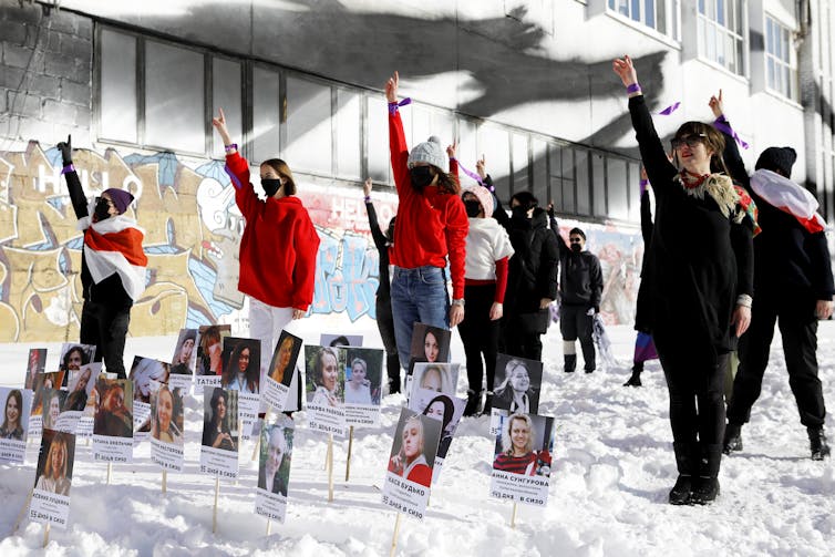 Mujeres vestidas de rojo se paran en la nieve, sosteniendo los puños en el aire, con fotos de otras mujeres