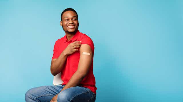 Person of colour showing off vaccination plaster on arm