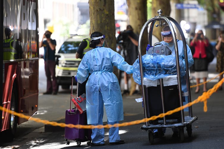 Workers dressed in PPE load luggage onto a bus.