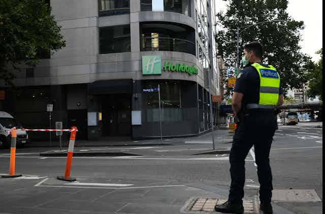 A police officer wearing a mask stands in front of the Holiday Inn in Melbourne's CBD.