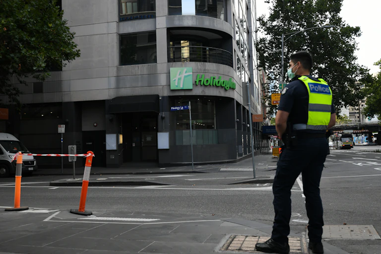A police officer wearing a mask stands in front of the Holiday Inn in Melbourne's CBD.